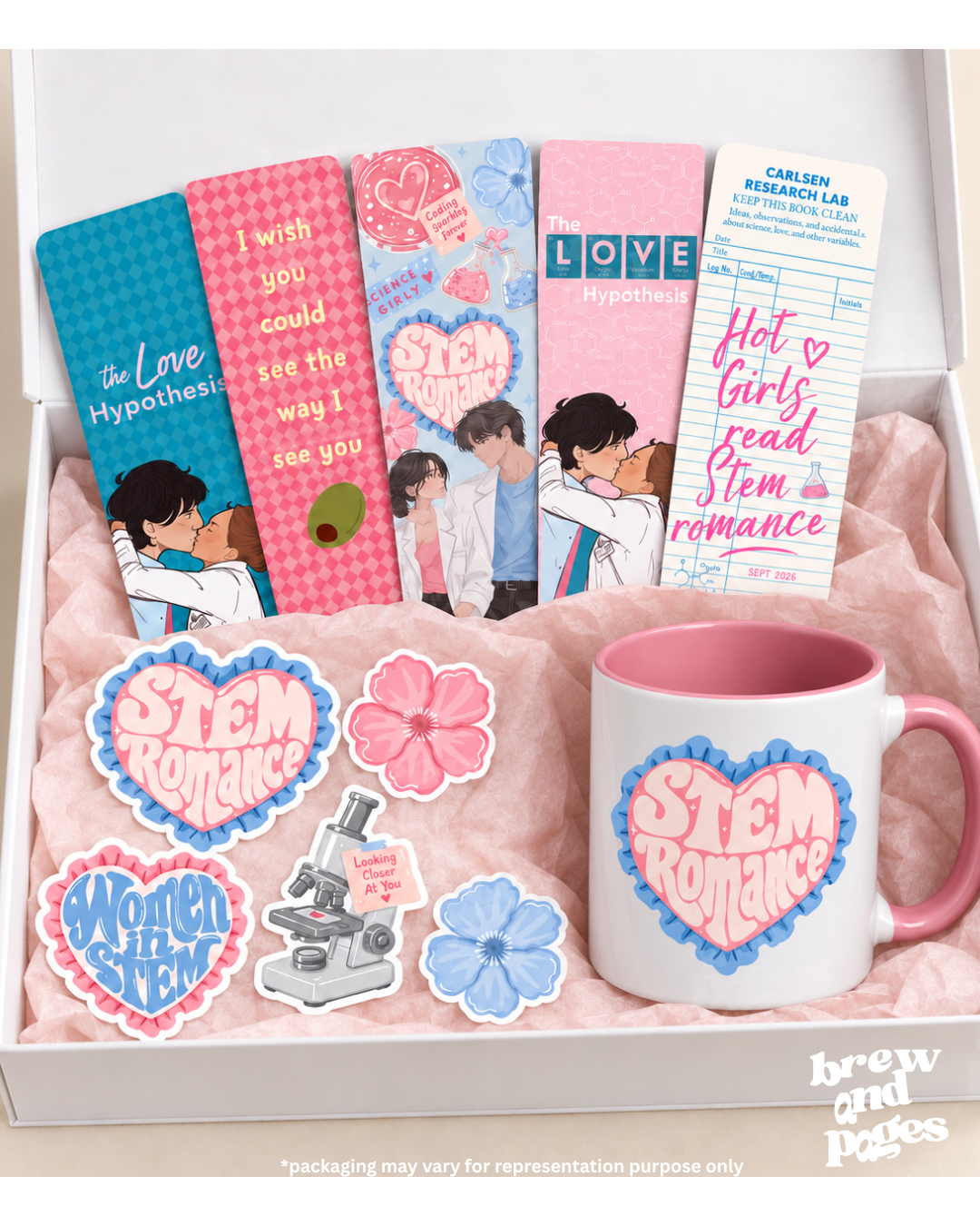 A boxed gift set featuring romance-themed STEM mugs, bookmarks, stickers, and a card. The set includes a white mug with a pink handle and pink interior, several pink and blue books or bookmarks with illustrated couples and text like 'STEM Romance' and 'LOVE Hypothesis,' flower-shaped stickers, a microscope sticker, and a 'Women in STEM' sticker, all arranged in a white box with pink tissue paper.