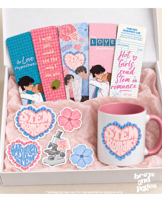 A boxed gift set featuring romance-themed STEM mugs, bookmarks, stickers, and a card. The set includes a white mug with a pink handle and pink interior, several pink and blue books or bookmarks with illustrated couples and text like 'STEM Romance' and 'LOVE Hypothesis,' flower-shaped stickers, a microscope sticker, and a 'Women in STEM' sticker, all arranged in a white box with pink tissue paper.